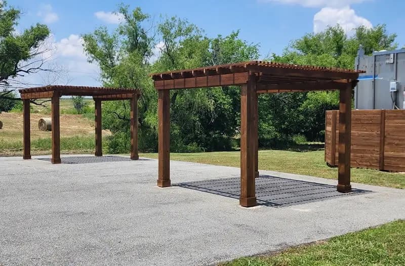 Two wood shade structures built beside a paved outdoor area